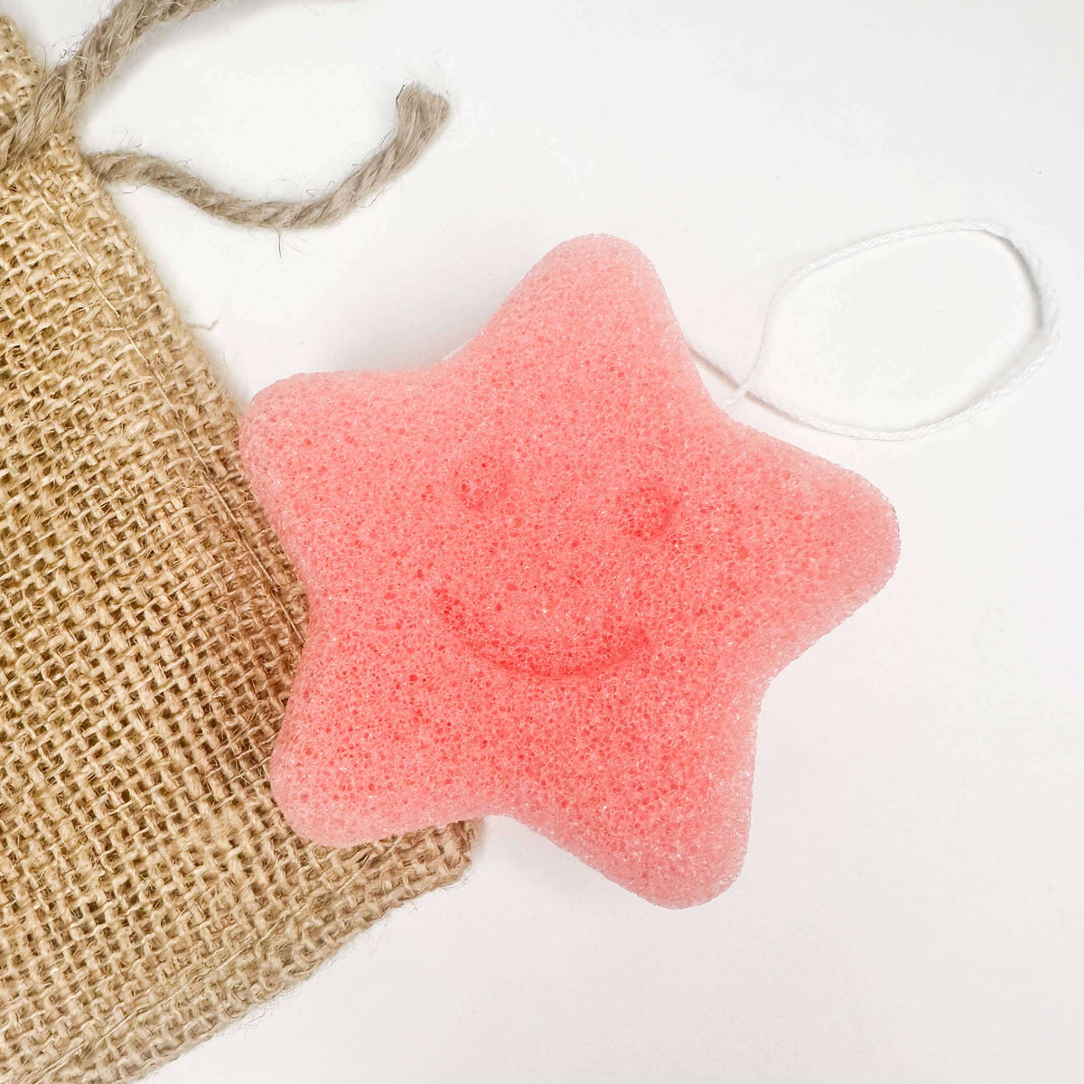 Natural Organic Konjac Facial Sponges in star shape, soft pink color, with a smiley face design, next to a burlap bag.
