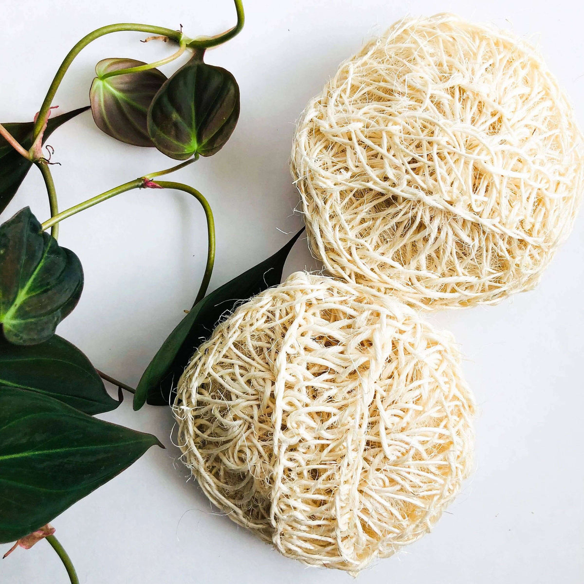 Two natural fiber balls on a white surface with green leaves.