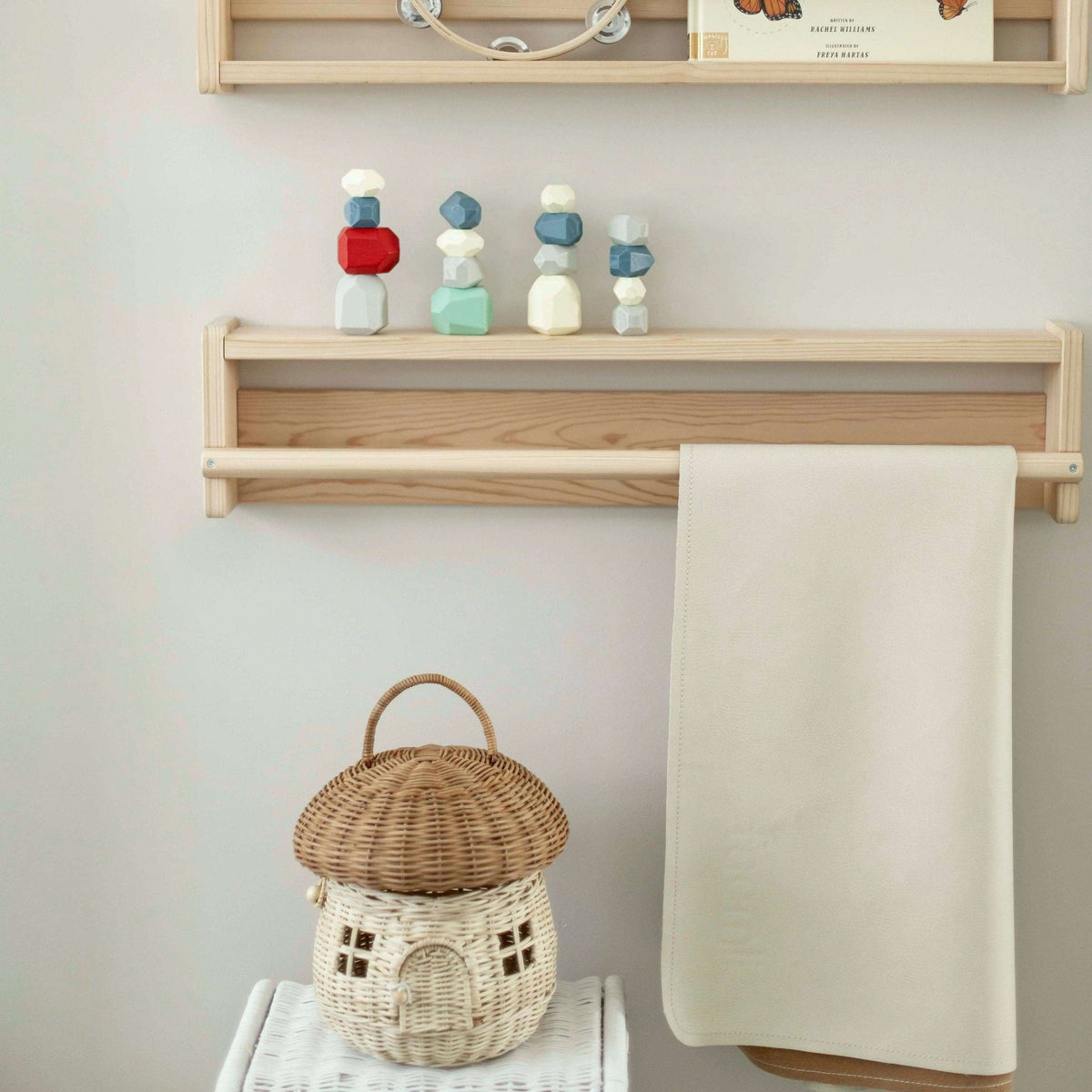 Wooden shelf with colorful wooden blocks, a woven basket, and a towel on a light gray wall.