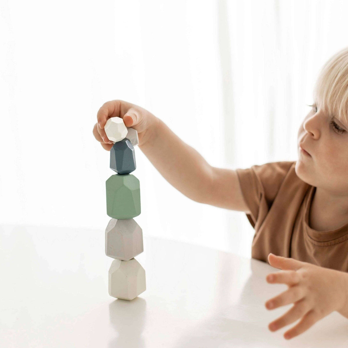 Child playing with colorful stacking blocks on a white surface