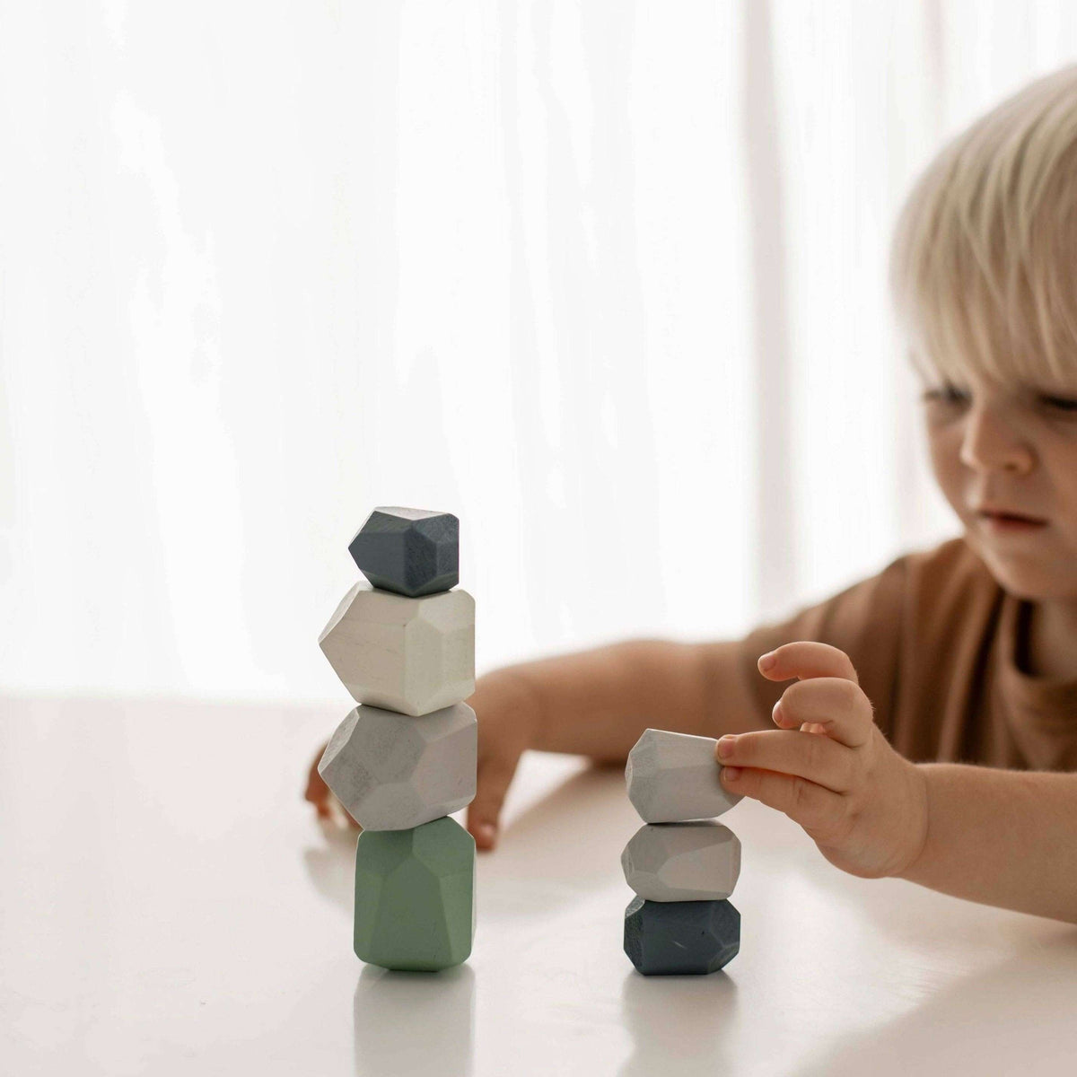 Child playing with geometric wooden blocks on a light surface.