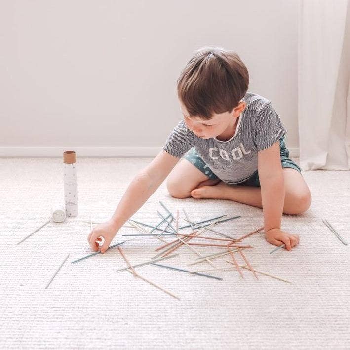 Child playing Pick Up Sticks on the floor, fostering concentration and family fun with colorful wooden sticks.