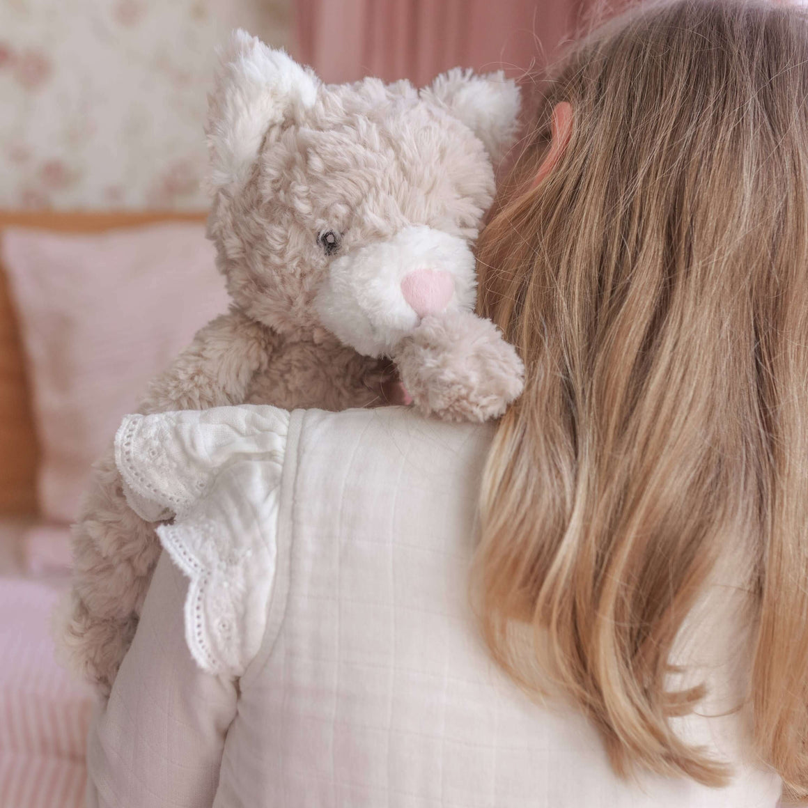 Child holding a teddy bear in a softly lit room with pink bedding.