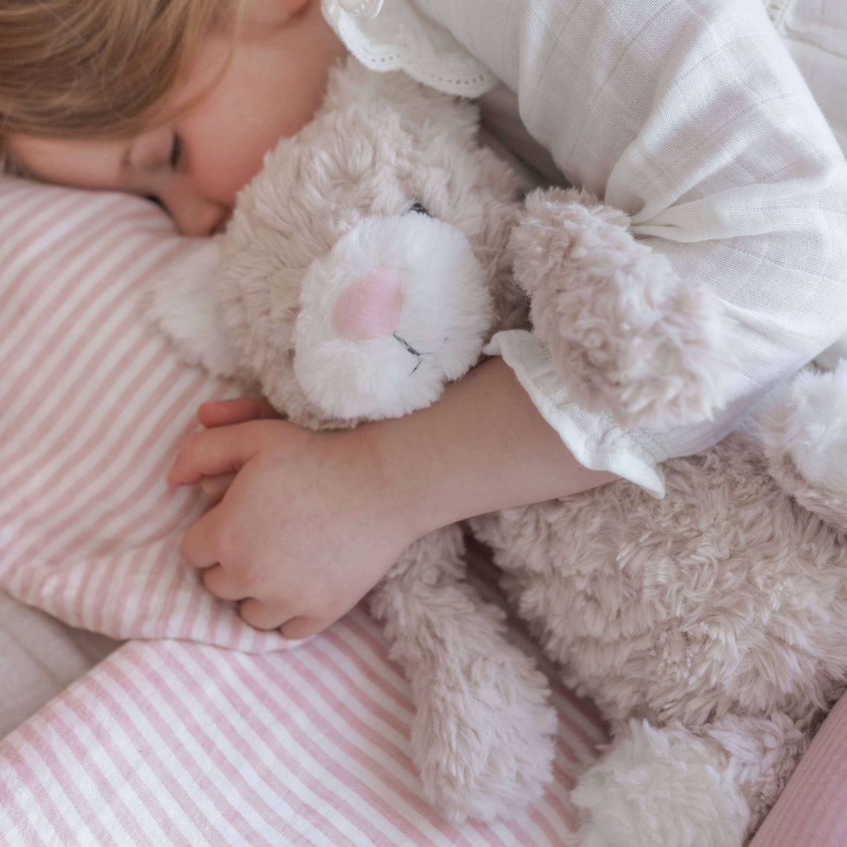 Child sleeping with a teddy bear on a pink striped bed