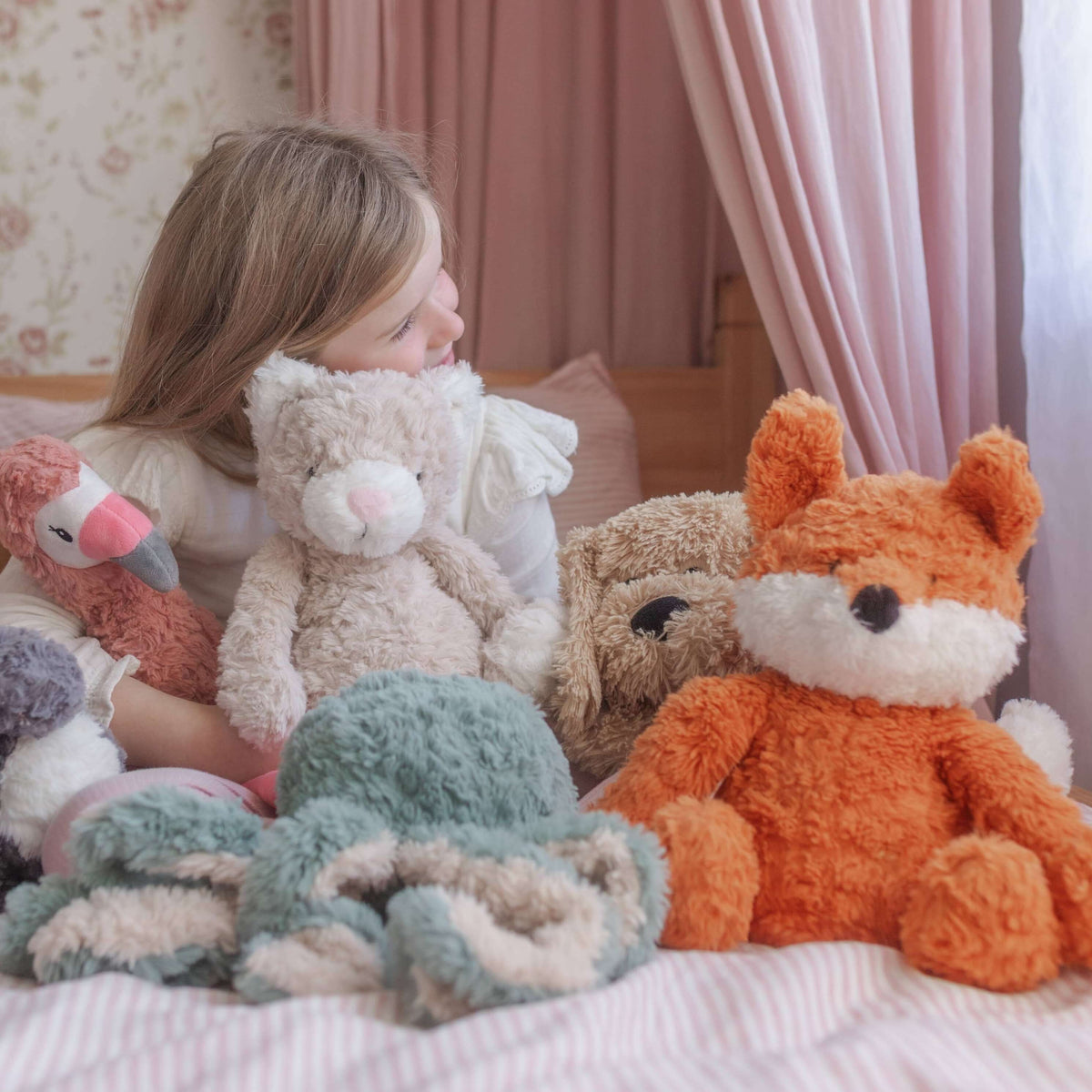 Child surrounded by stuffed animals on a bed in a bedroom setting