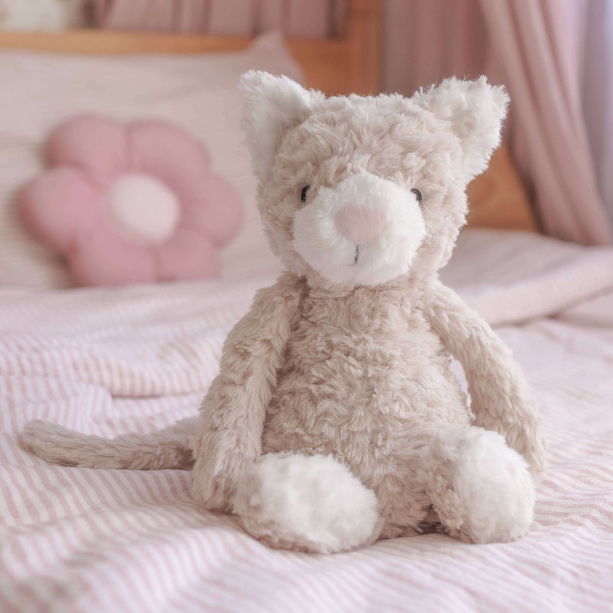 Plush cat toy on a bed with pink bedding and curtains