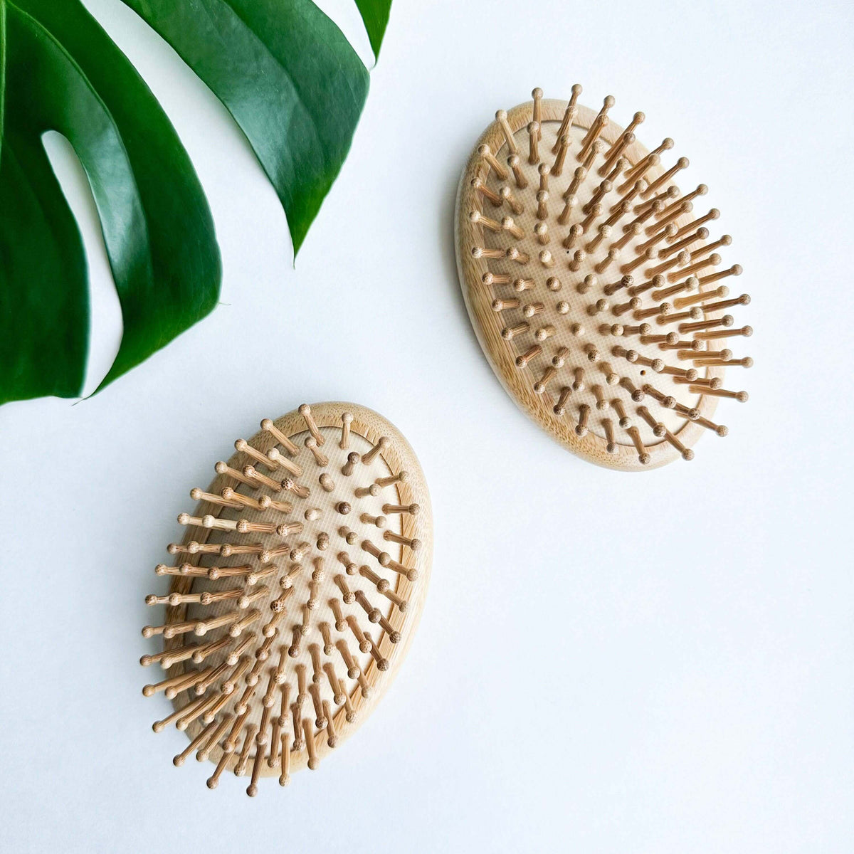 Two wooden hairbrushes on a light surface with a green leaf in the corner.