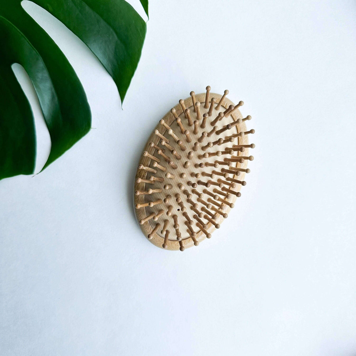 Wooden hairbrush on a white surface with a green leaf in the corner