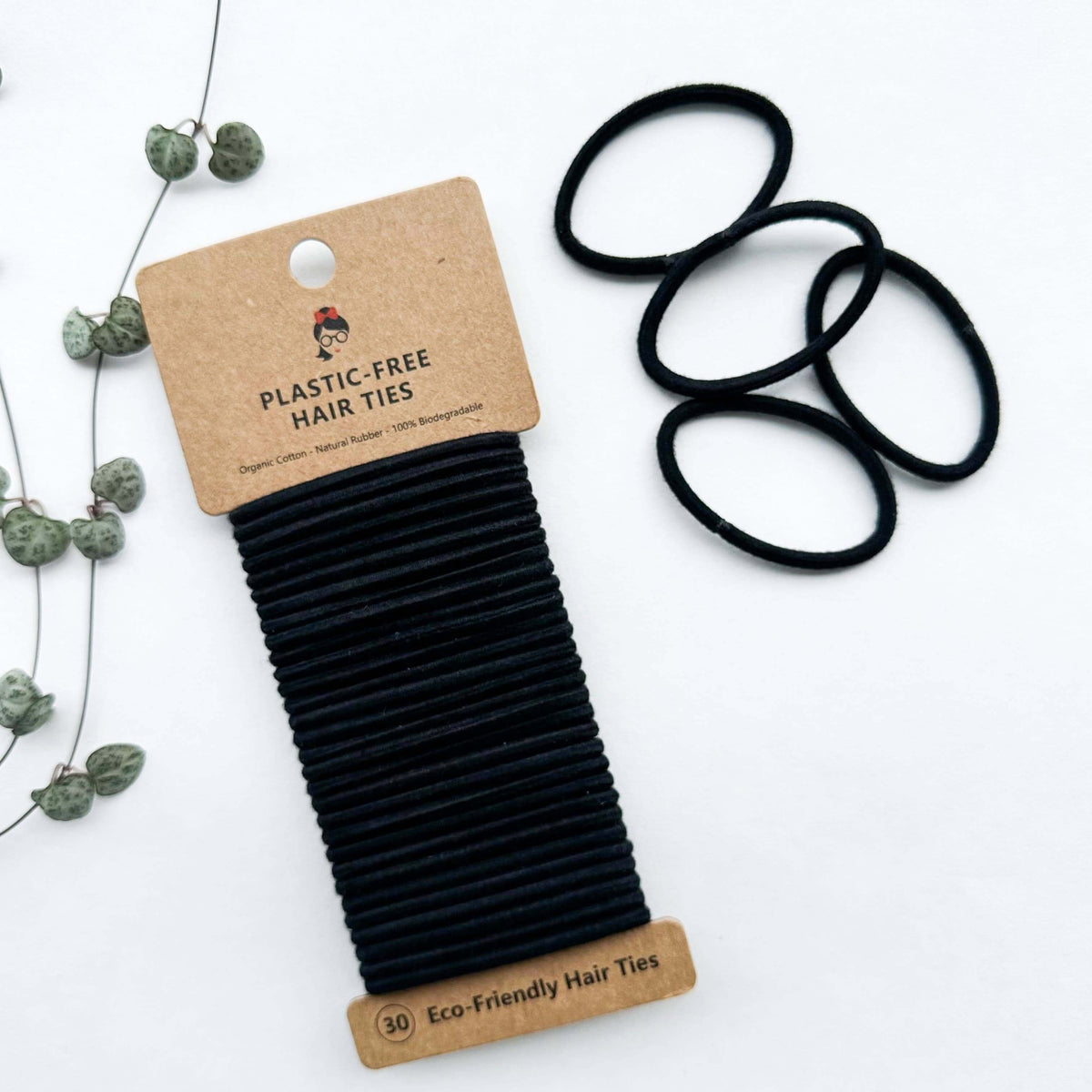 Black hair ties on a cardboard holder with 'Plastic-Free Hair Ties' label on a white background.