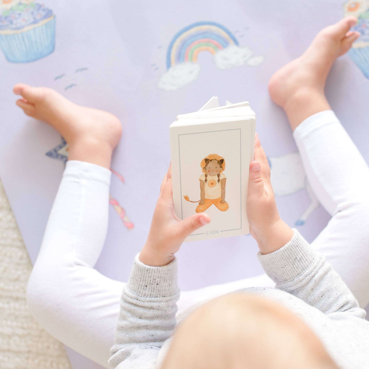 Child holding a book with a lion illustration on a colorful floor mat.