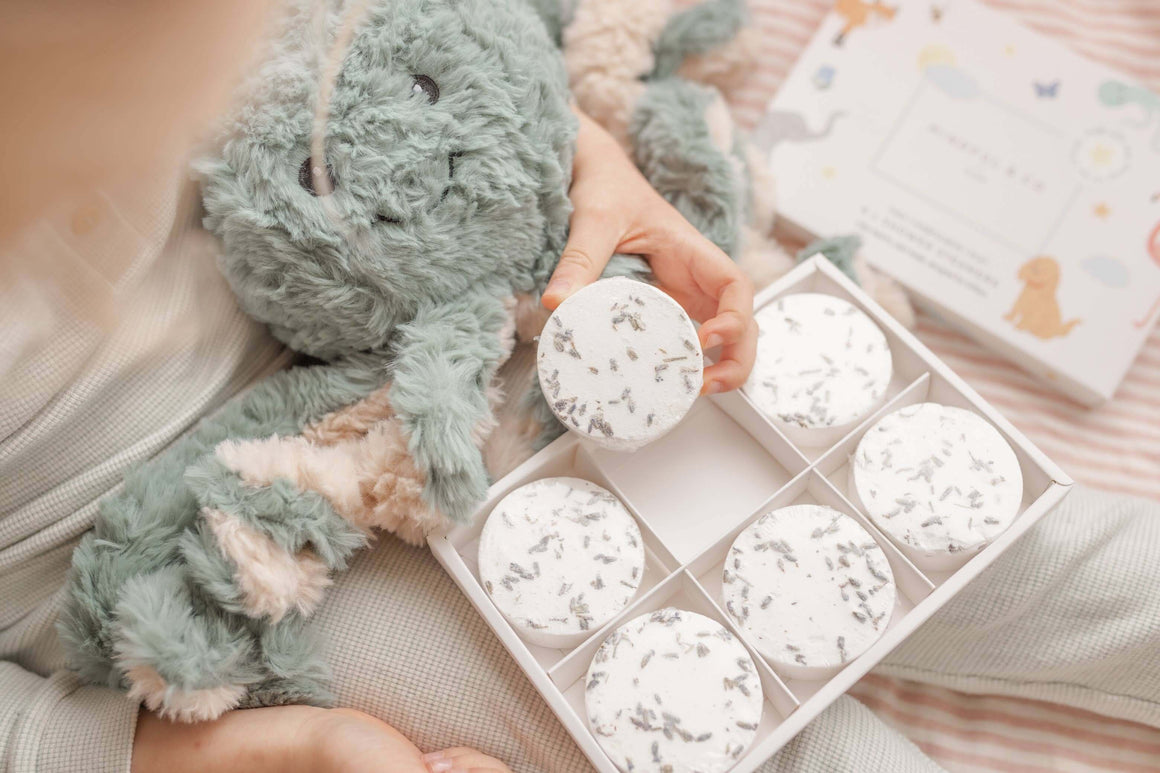 Child holding Sensory Shower Steamers x 6 box with soothing lavender shower tablets and plush toy.