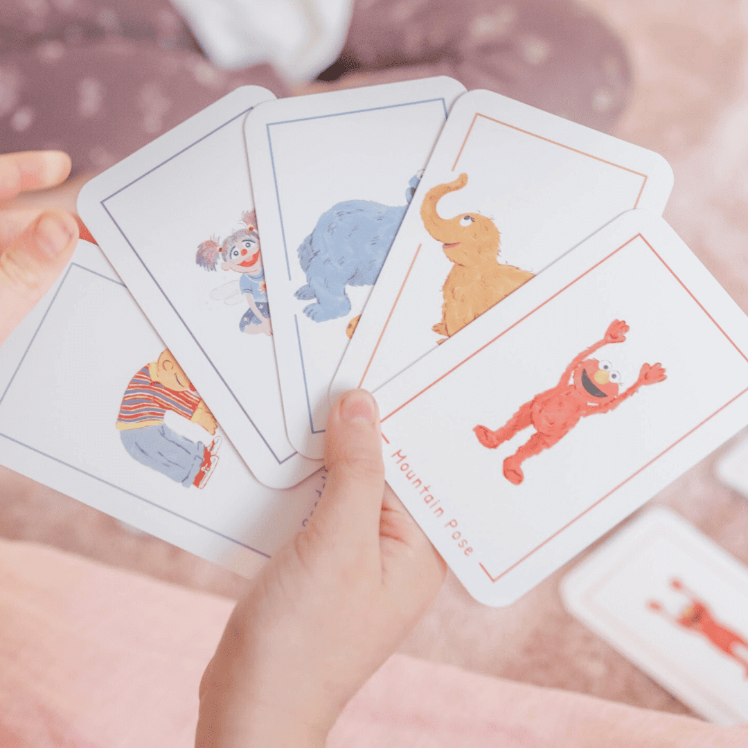 Child's hands holding colorful cards from the Sesame Street 3-in-1 Card Game featuring fun characters.