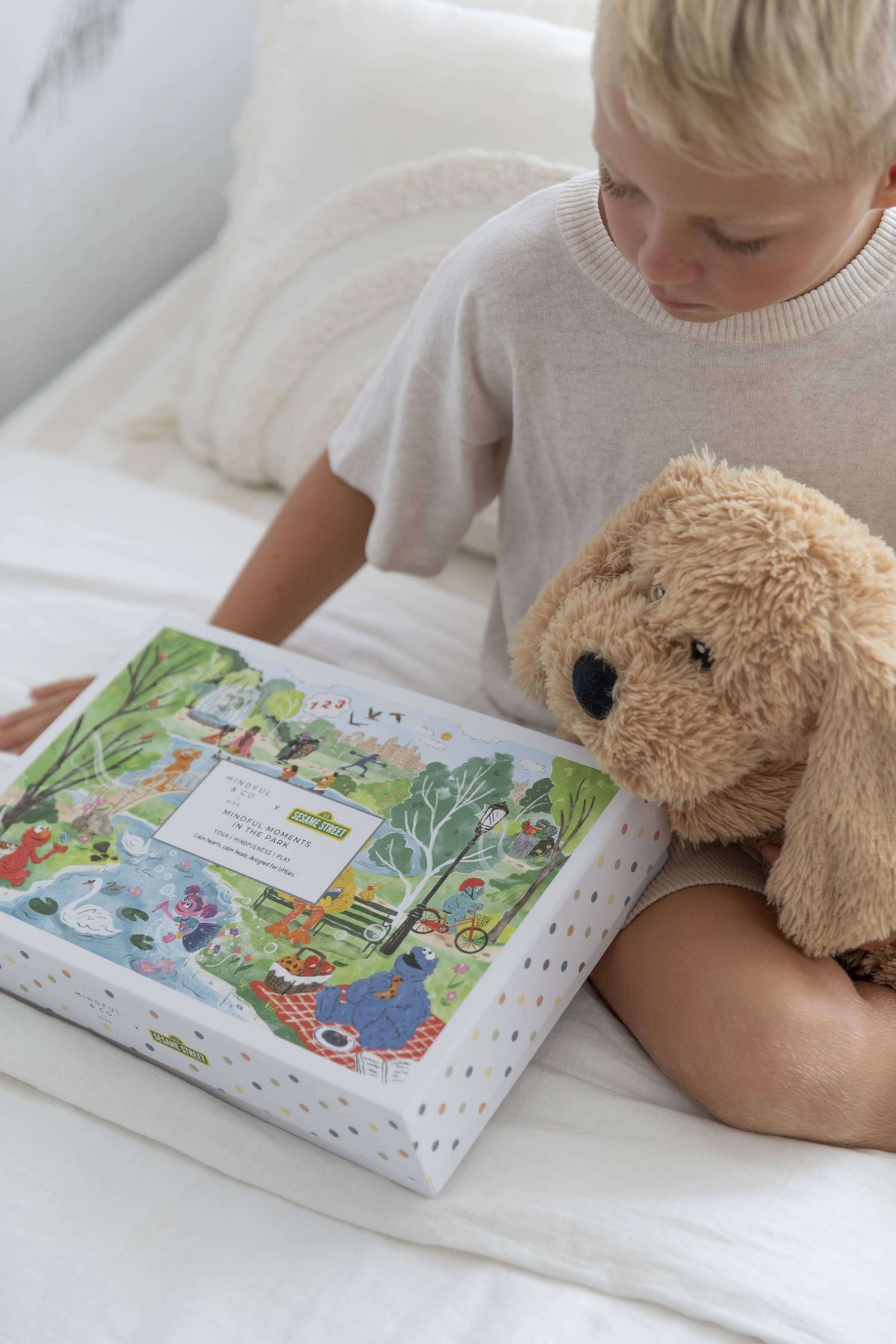Child with a teddy bear, excitedly holding the Mindful Moments with Sesame Street Floor Puzzle box.