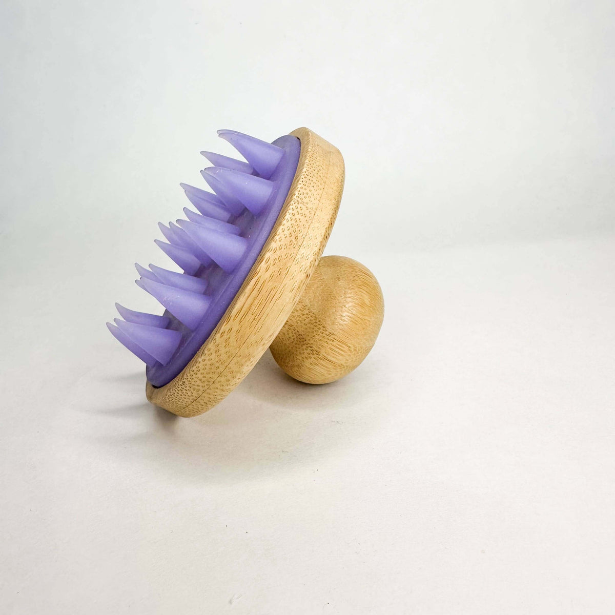 Purple silicone scrubber on a wooden handle against a white background