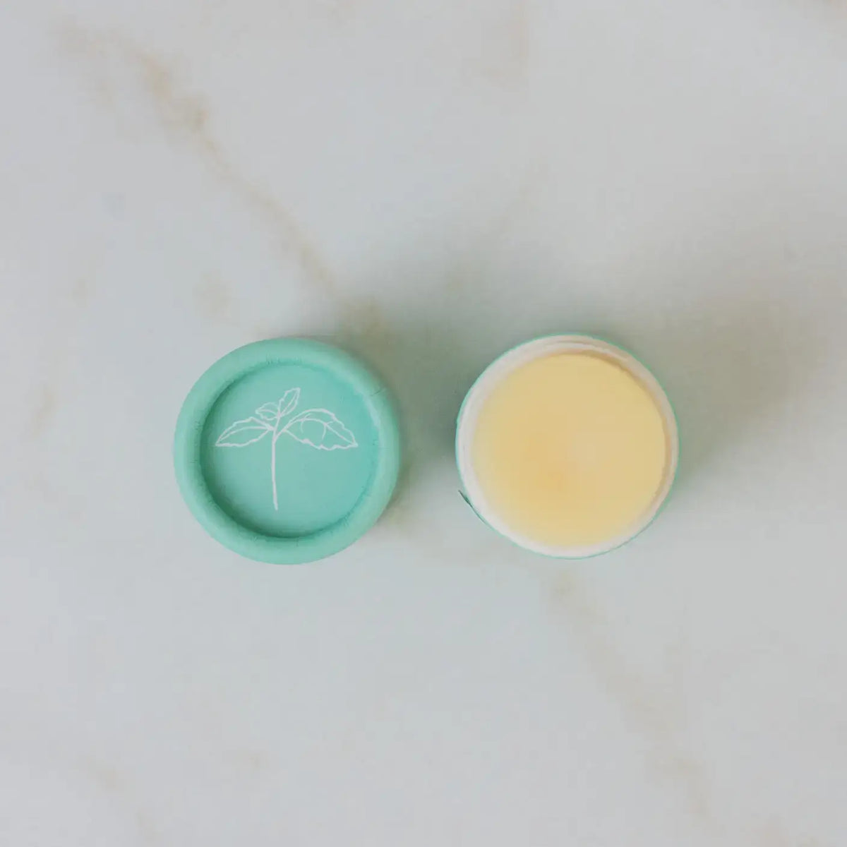 Two small containers, one green with a lid and one yellow without a lid, on a light marble background.