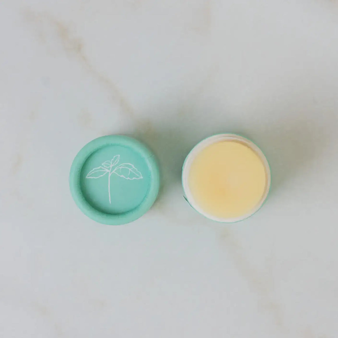 Two small containers, one green with a lid and one yellow without a lid, on a light marble background.