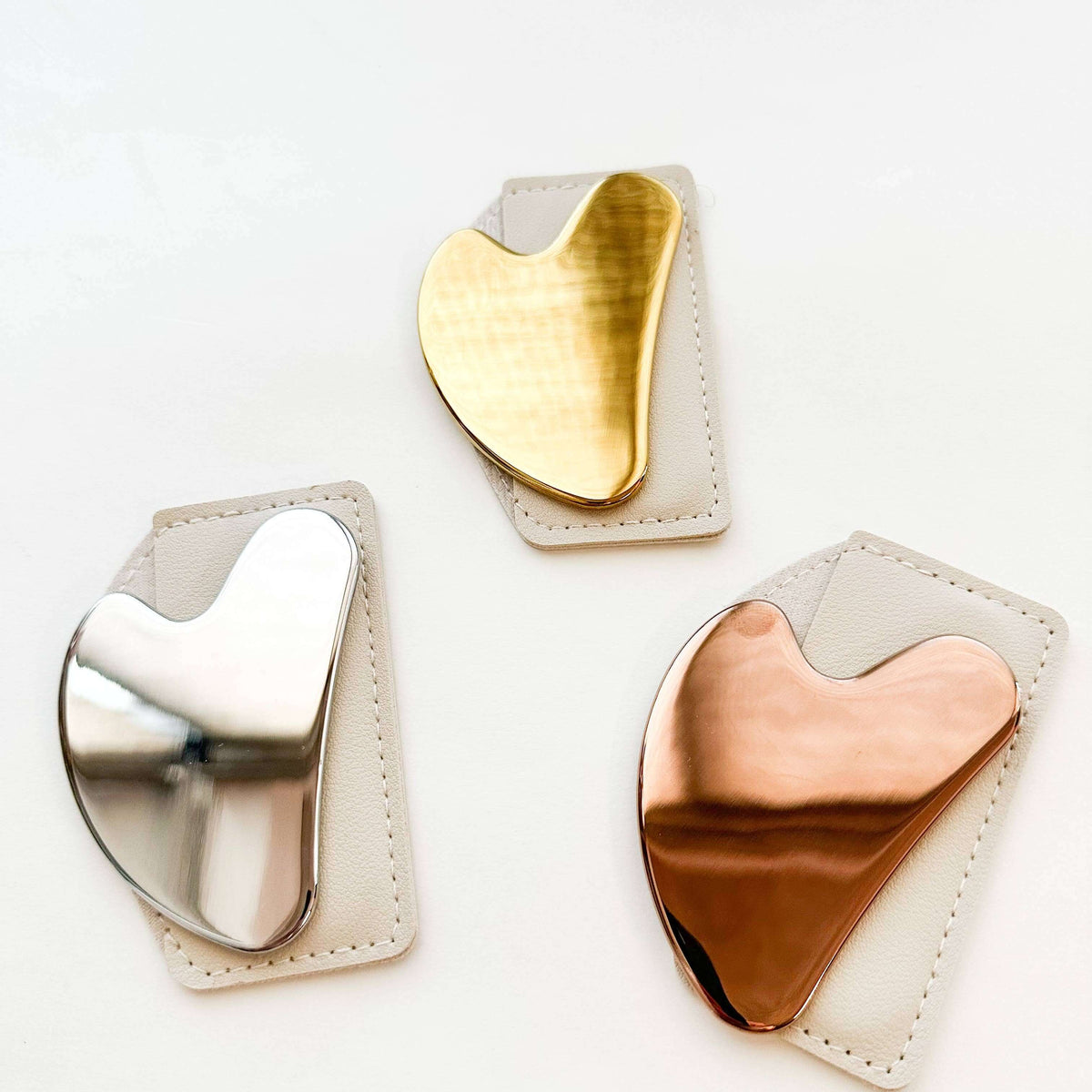 Three heart-shaped metal tools on beige pads with gold, silver, and rose gold finishes.