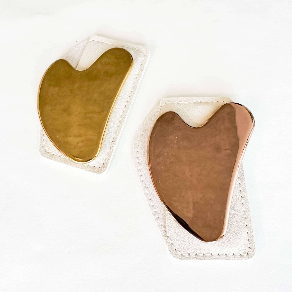 Two heart-shaped gua sha tools, one gold and one rose gold, on a white background.