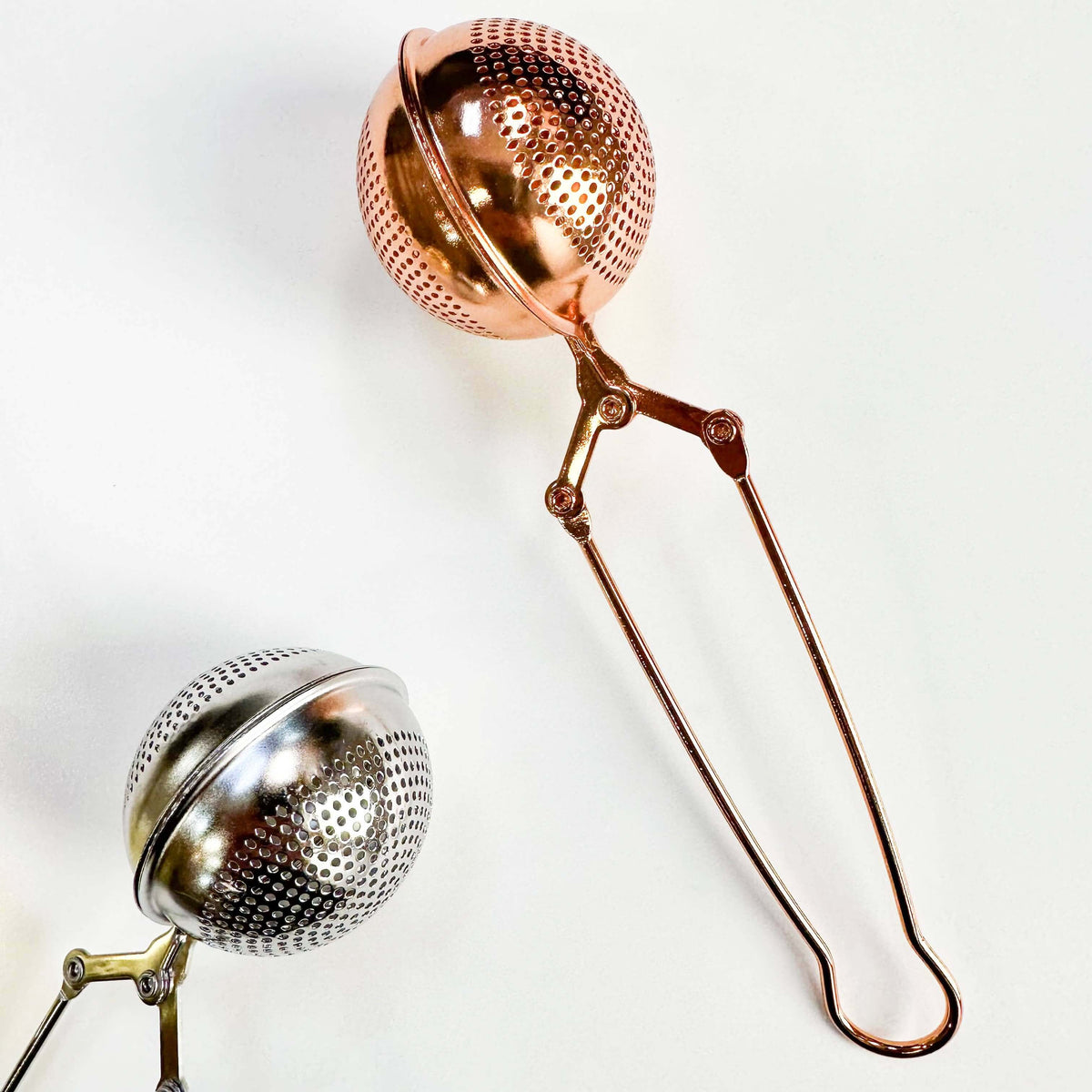 Copper and silver tea infusers on a white background