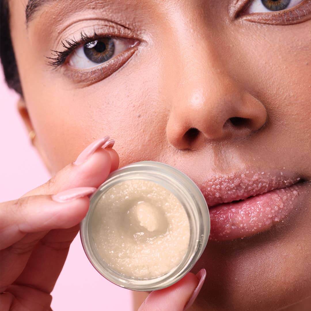 Close-up of a woman holding a jar of cream near her face against a pink background