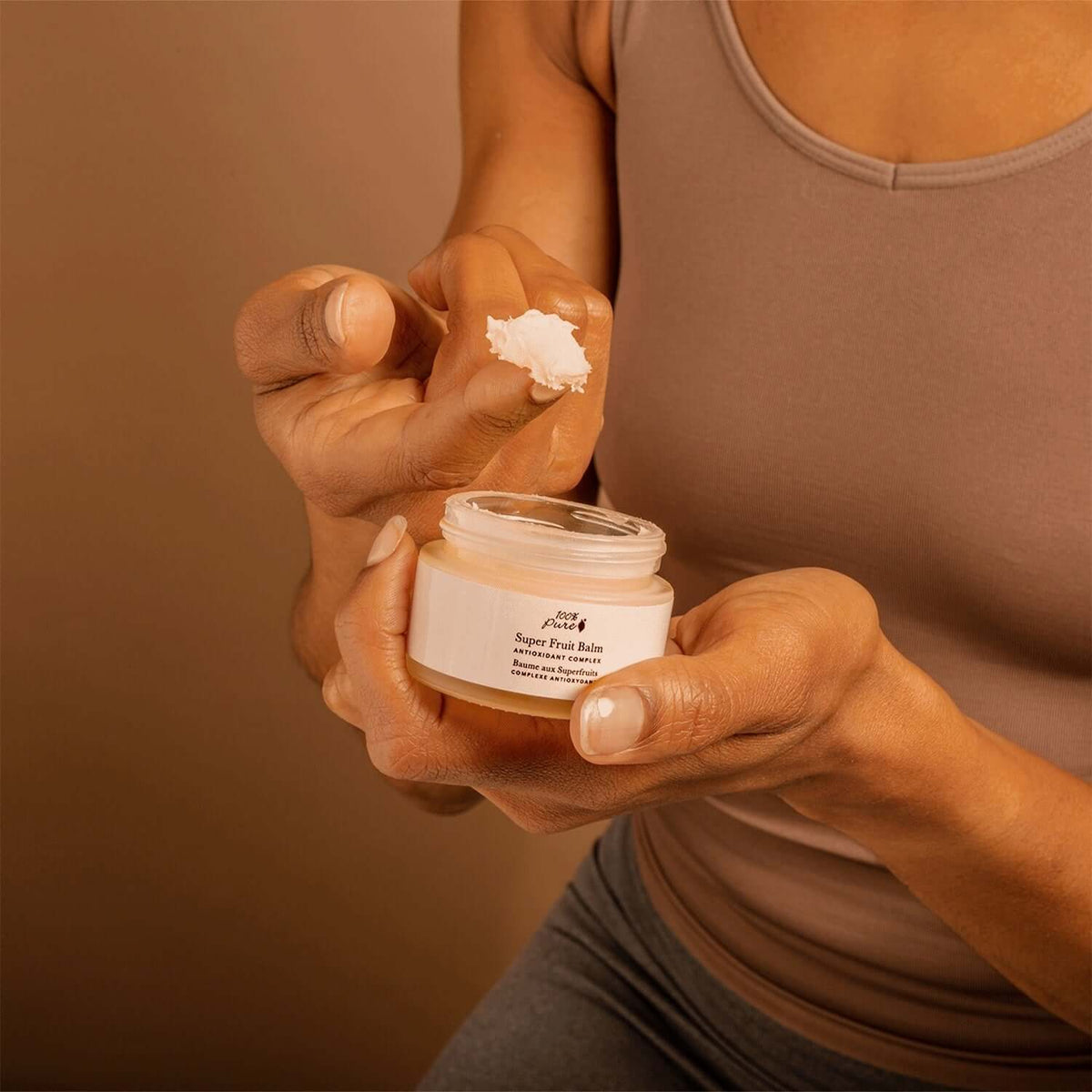 A person applying Super Fruit Balm from a jar, showcasing its creamy texture for nourishing skin.