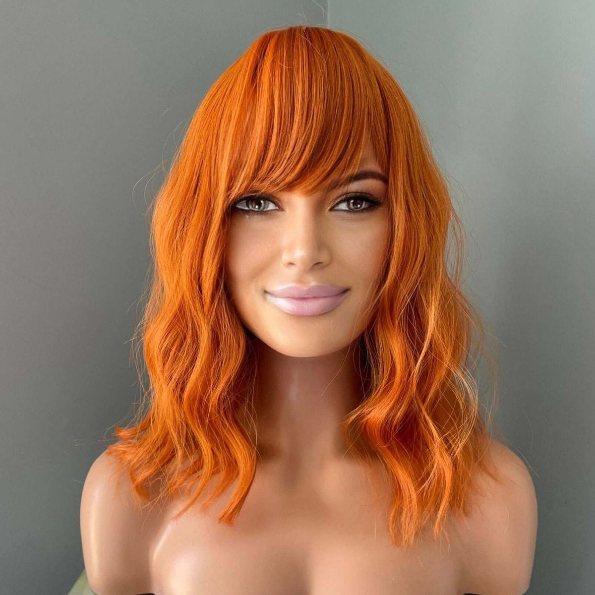 Orange Wig with Bangs displayed on a mannequin featuring vibrant tangerine color and soft body waves.