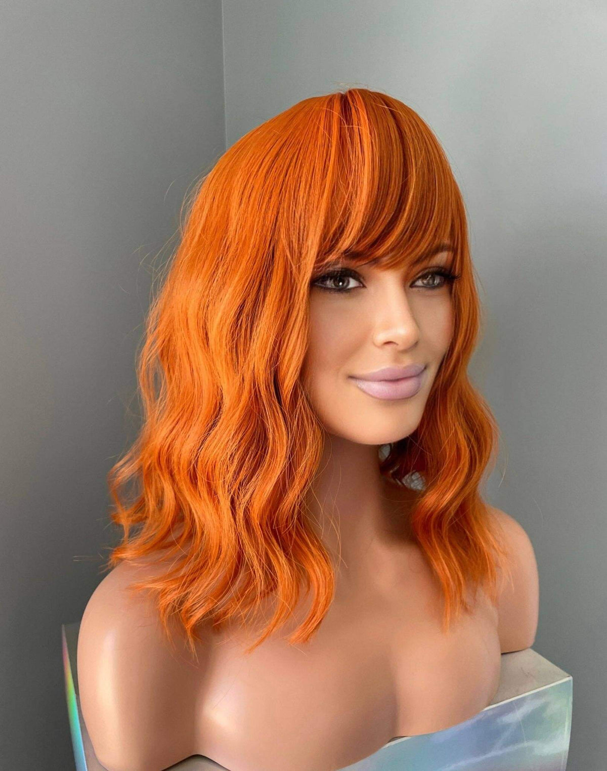 Tangerine Short Orange Wig with Bangs styled on a mannequin, showcasing vibrant color and soft body waves.