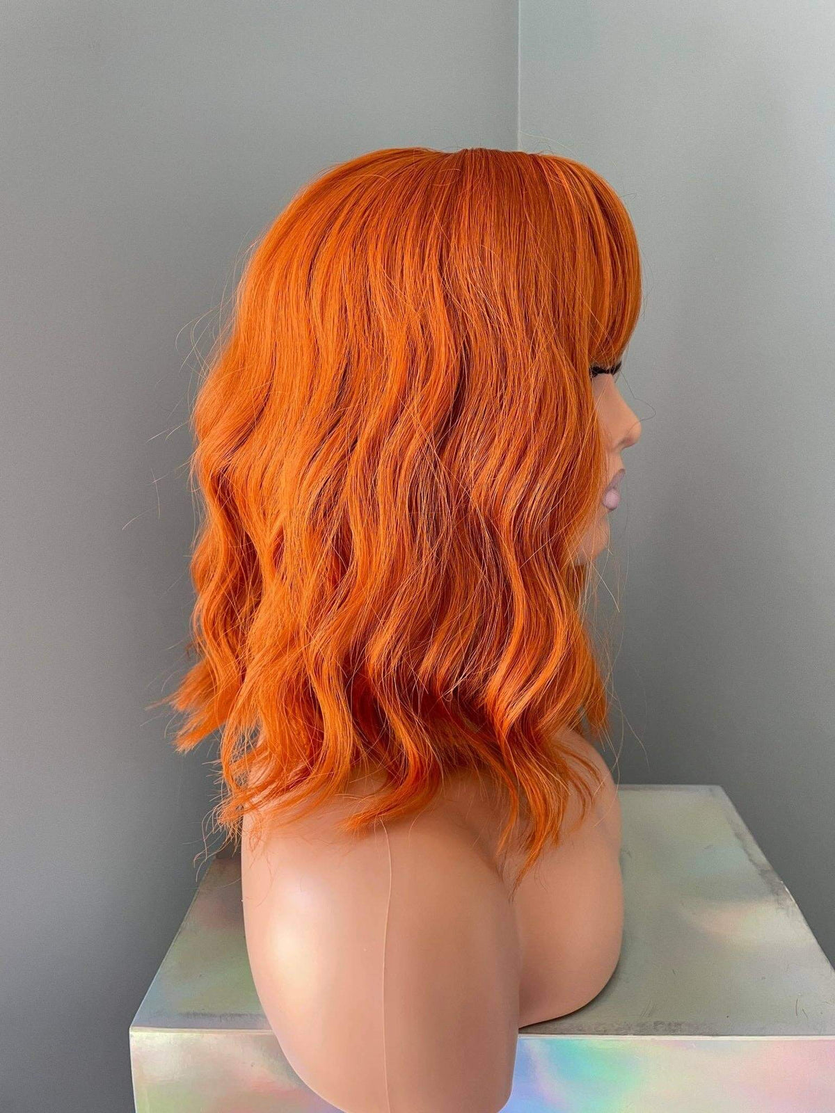 Orange Wig with Bangs displayed from the side, showcasing vibrant tangerine color and soft waves.