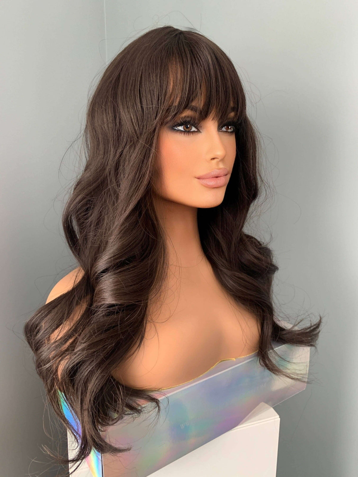 Tasha Long Dark Chocolate Brown Wig with Bangs displayed on a mannequin, featuring soft waves and a full fringe.