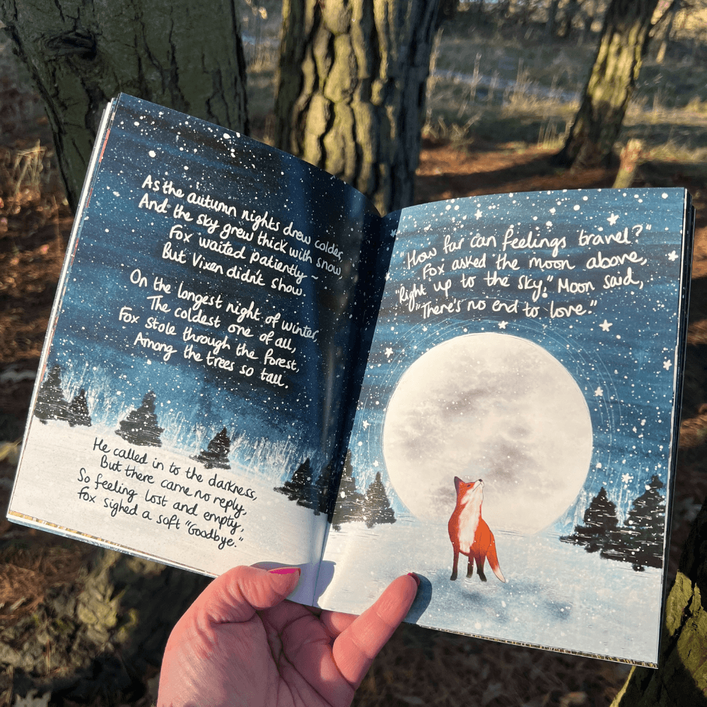 The Longest Night Paperback Book + bookmark open to a page with a fox and a full moon in a starry night sky.