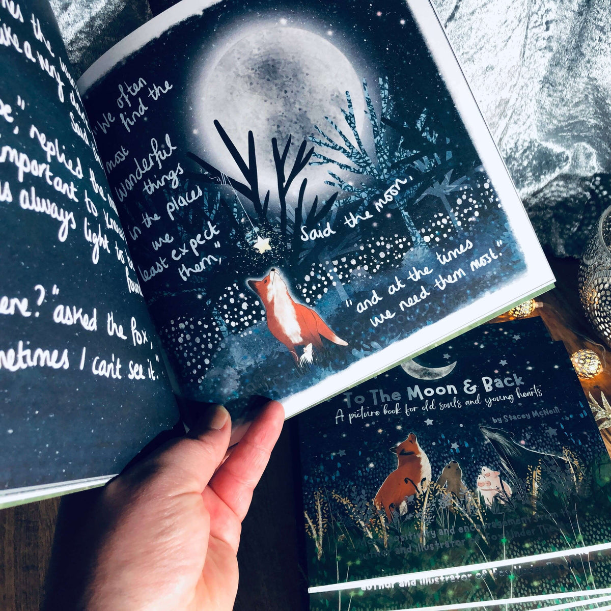 Hands holding open a page of 'To The Moon & Back - Fox Under The Moon - 2' featuring Fox and the Moon.