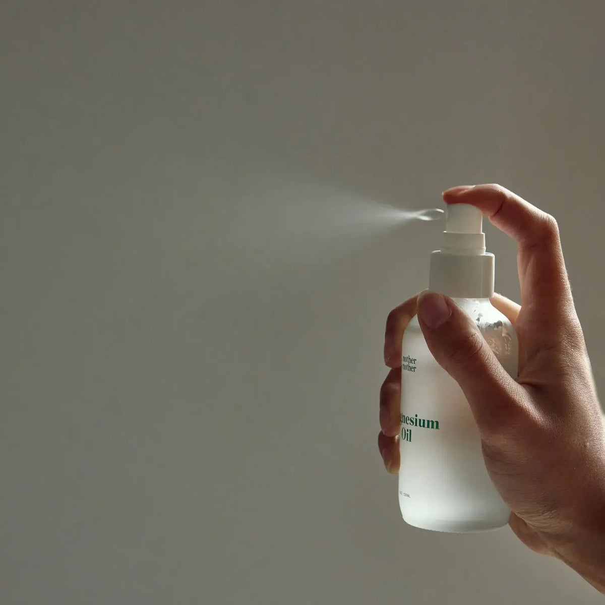 Hand holding a spray bottle with a mist being released against a plain background