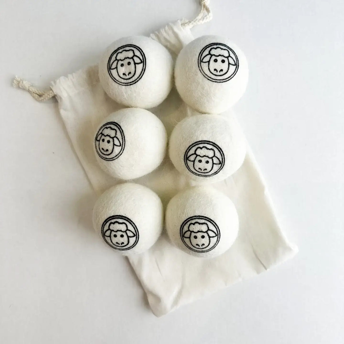 Set of six white laundry detergent pods with black sheep faces in a drawstring bag on a light background