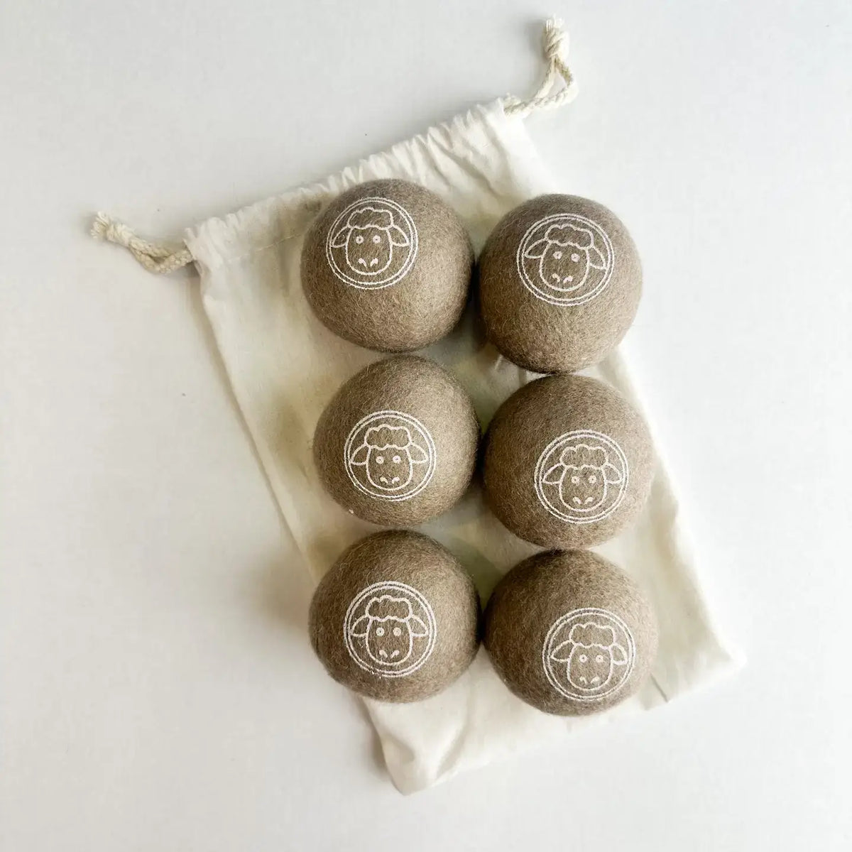 Set of six brown laundry detergent pods with a sheep logo in a white drawstring bag on a light background