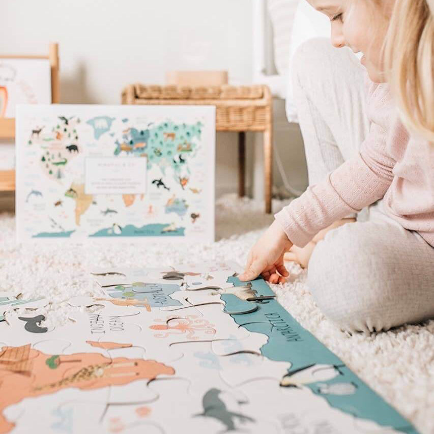 Child engaging with the World Map Floor Puzzle while seated on a plush rug, surrounded by educational materials.