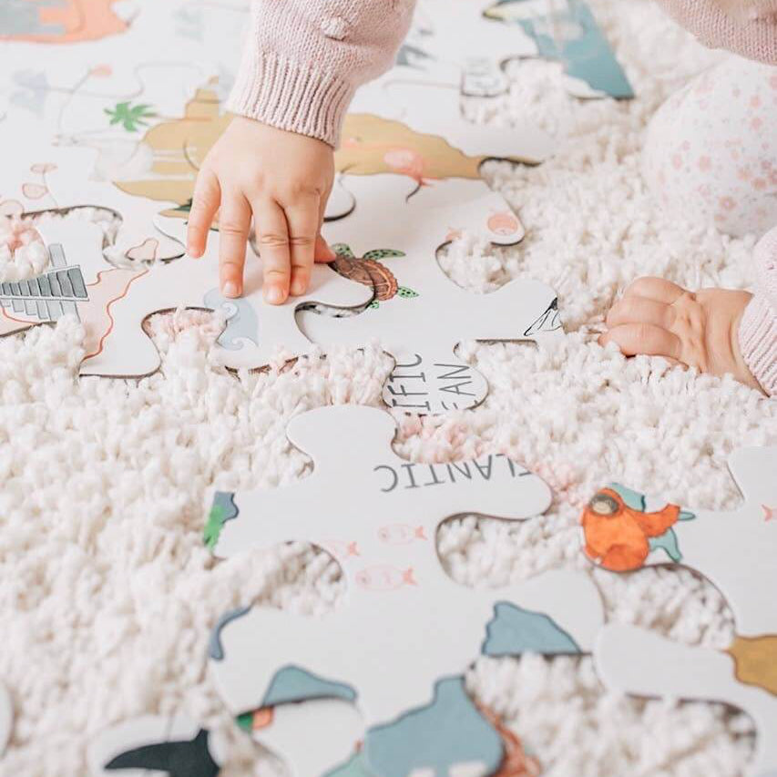 Child's hand assembling the World Map Floor Puzzle on a soft carpet, fostering learning and creativity.