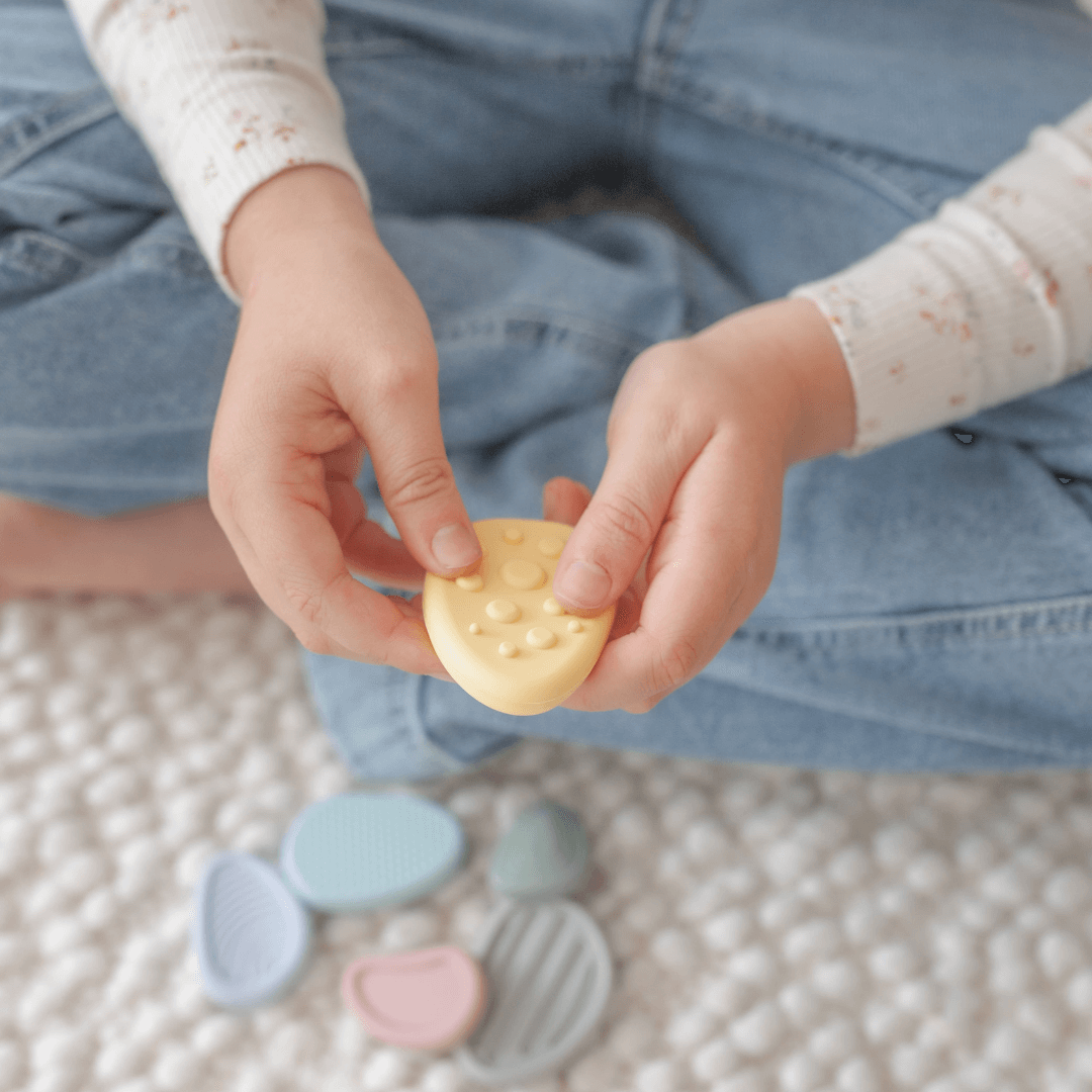 Child holding a yellow Worry Stone from the Calming Sensory Fidget for Kids (Set of 6) on a textured surface.