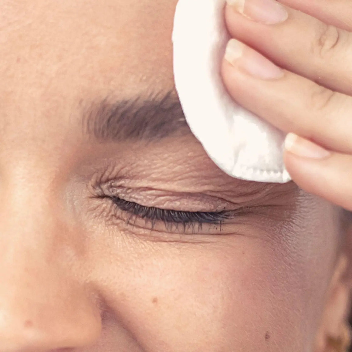 A woman applying Glow Tonic with a cotton pad to achieve radiant, even skin tone.