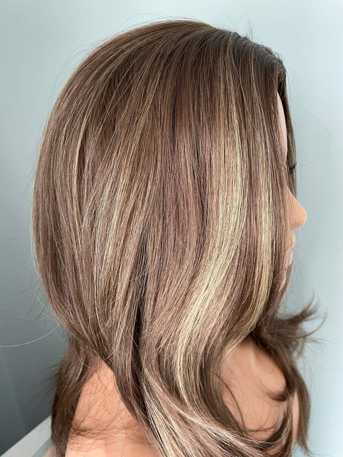Close-up of a person with brown hair with blonde highlights against a light gray background