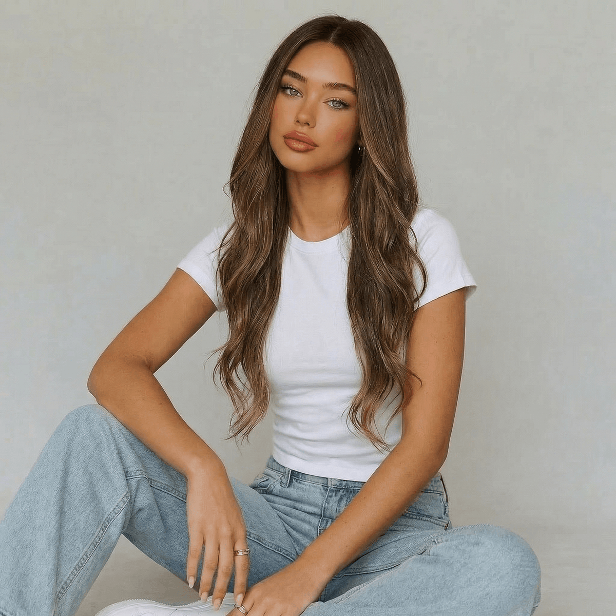 Model wearing a long highlighted brown body wave wig with soft waves, dressed in a white t-shirt and blue jeans.