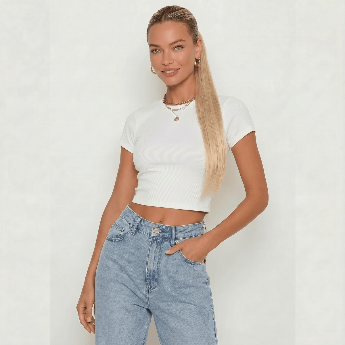 Model wearing a white cropped top with jeans and long silky straight hair featuring a buttery blonde ponytail hair extension.