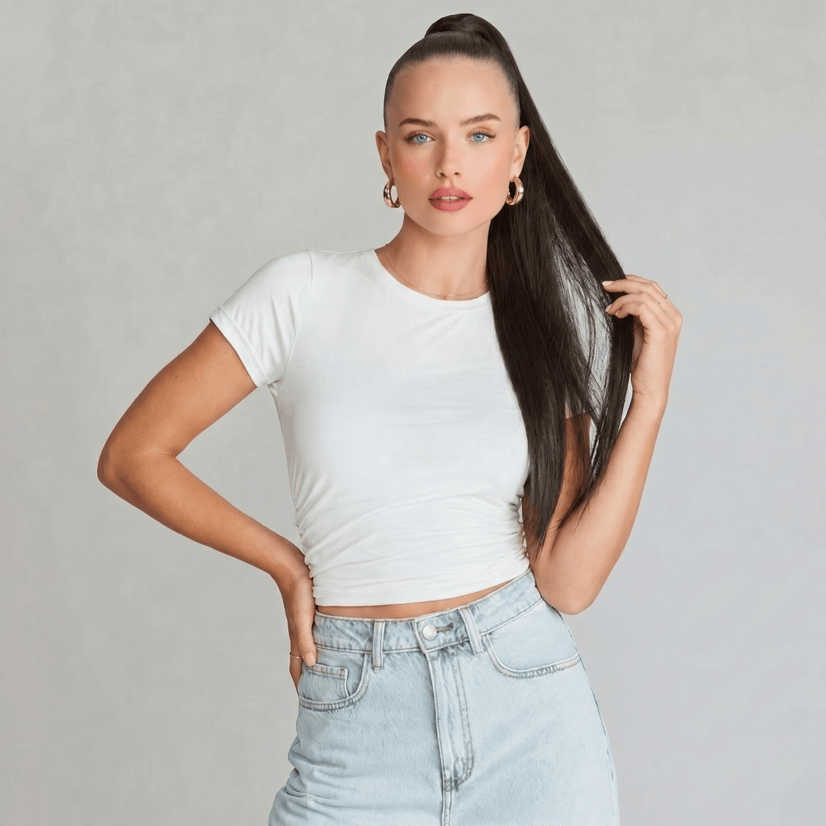 Model wearing a white t-shirt and high-waisted jeans showcasing a chocolate brown ponytail hair extension.