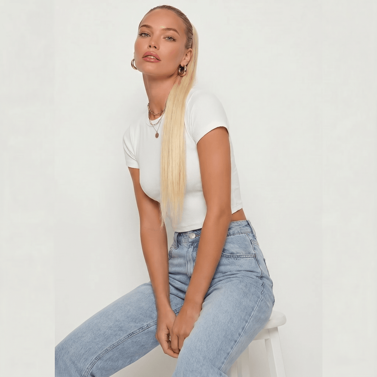 Model showcasing a platinum blonde ponytail hair extension with a stylish white crop top and light blue jeans.