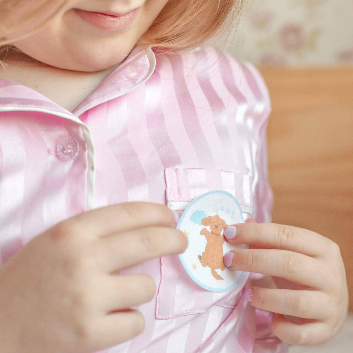 Child holding a round badge with a bear design on a pink shirt.