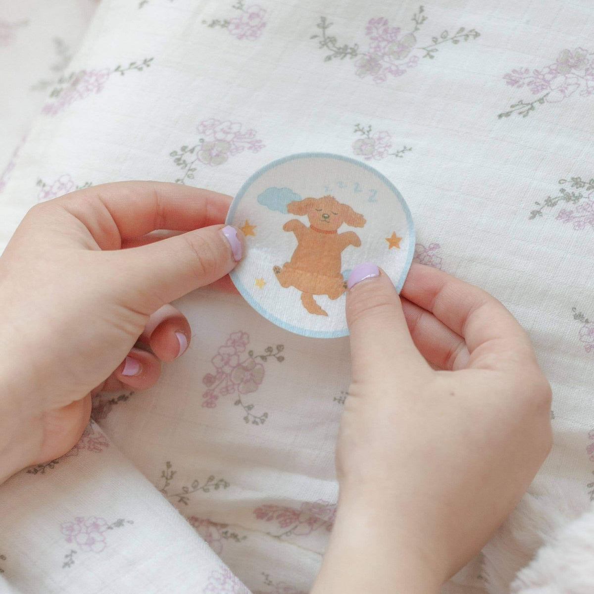 Hand holding a round sticker with a cartoon dog on a floral fabric background