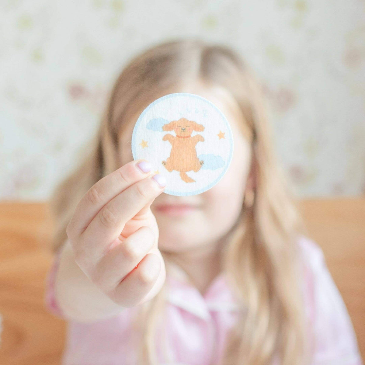 Person holding a round sticker with a cartoon dog design against a blurred background