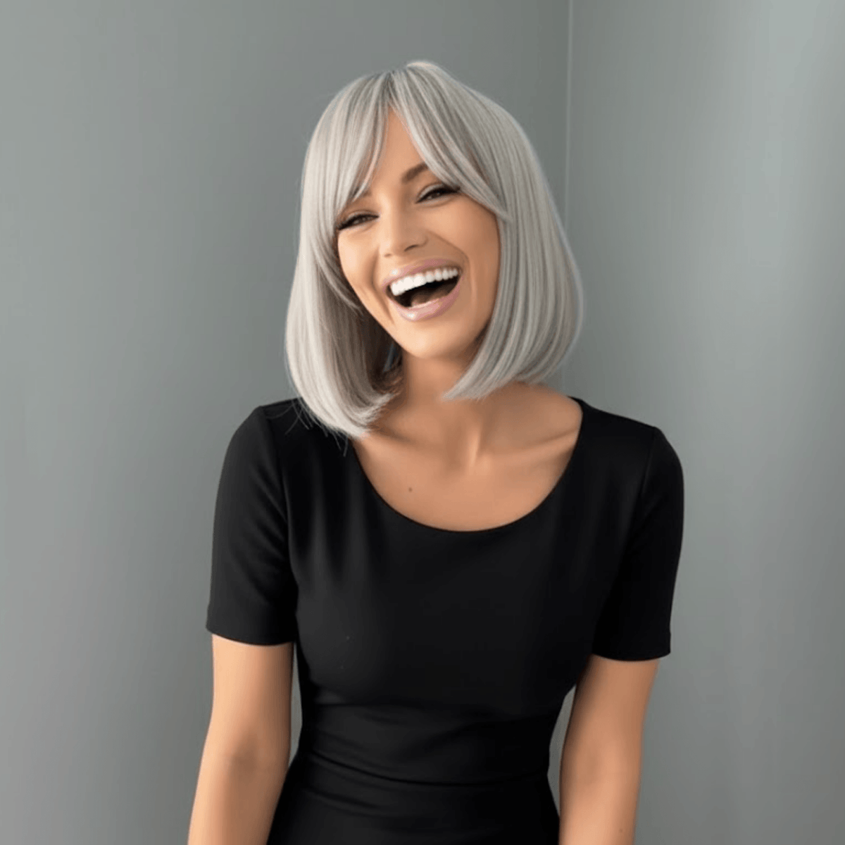 A woman with a short, straight, silver-gray wig and bangs is shown from the chest up, wearing a black short-sleeve top against a plain gray background.