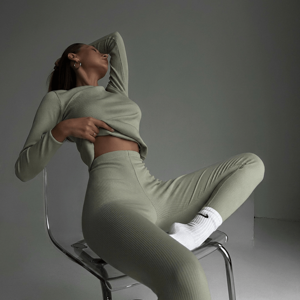Woman in a green outfit sitting on a chair against a gray background